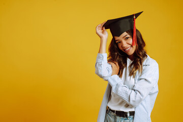 Portrait of African American girl in a graduation hat on her head posing on a yellow background....