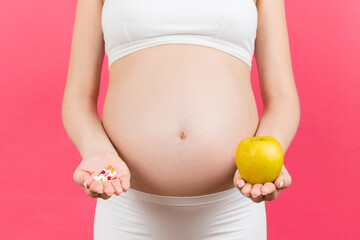 Close up of an apple and a heap of pills in pregnant woman's hands at colorful background with copy space. Making a choice during pregnancy concept