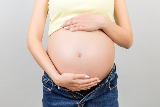 Cropped image of pregnant woman in unzipped jeans showing her baby bump at colorful background with copy space. Waiting for a baby concept