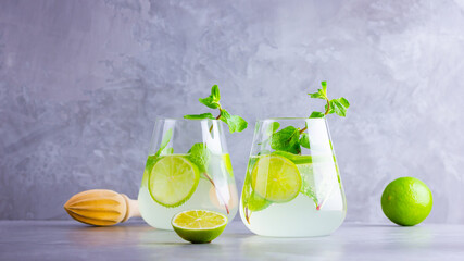 Cocktail mojito with lime and mint in glass. Two glasses of mojito on a gray background. Refreshing mint cocktail with lime. Infused water