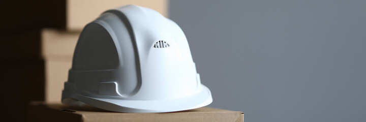 Fototapeta premium Cardboard box lies white protective helmet builder. Providing workers with personal protective equipment. White helmet for head or public inspector. Compliance by employees with safety regulations