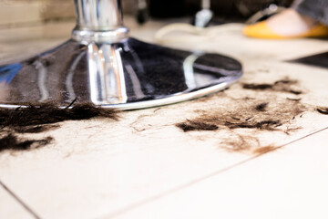 Cut brown hair lying on floor near metal barber chair. Saloon need cleaning service