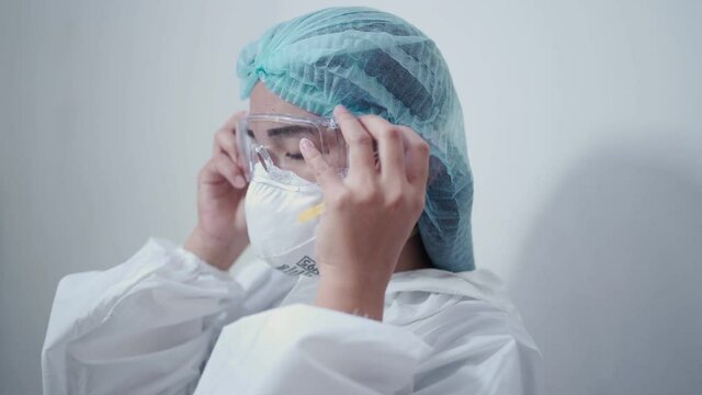 Asian female nurse wearing white ppe suit, medical protective suit, protective glasses, n95 mask and face shield pandemic covid-19 corona virus, in the medical clinic, infectious disease prevention