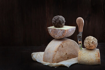 Fototapeta na wymiar Heads of hard home-made cheese lie on a napkin. Photo on a dark background. Cheese knife. The concept of still life. Copy of the space.