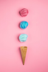 Colorful woolen balls entering the ice cream cone. Summer-inspired minimalistic photography. Empty waffle horn on a bright pink background with woolen balls. Deconstructed ice cream concept.