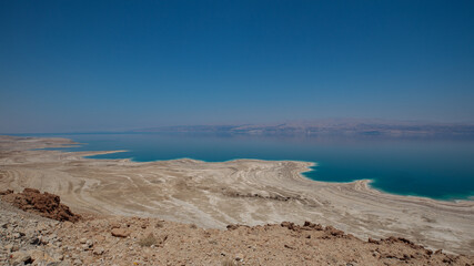 Fototapeta na wymiar Dead sea landscape wide angle shot. Dessert terrain with sinkholes in the foreground and mountains of Jordan in far background.