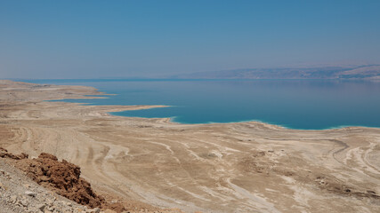 Dead sea landscape wide angle shot. Dessert terrain with sinkholes in the foreground and mountains of Jordan in far background.