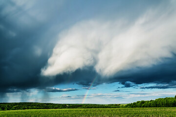 Naklejka na ściany i meble Rainclouds and rain over the field with rainbow