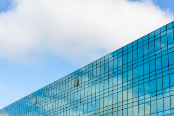 Low angle view of modern office building covered with glass. Blue sky with some white clouds in the background. Corporate Buildings Theme.