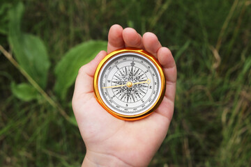Old classic navigation compass in hand on natural background as symbol of tourism with compass,...