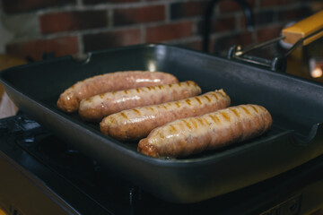 German sausages are grilled with tomatoes in oil. Grill pan on portable tile, gas