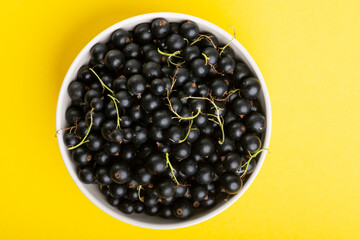 Black currant in a plate on yellow background. Top view. Flat lay
