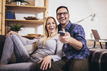 Obraz premium Cheerful couple is watching tv together and having fun in the living room.