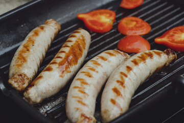 German sausages are grilled with tomatoes in oil. Grill pan on portable tile, gas
