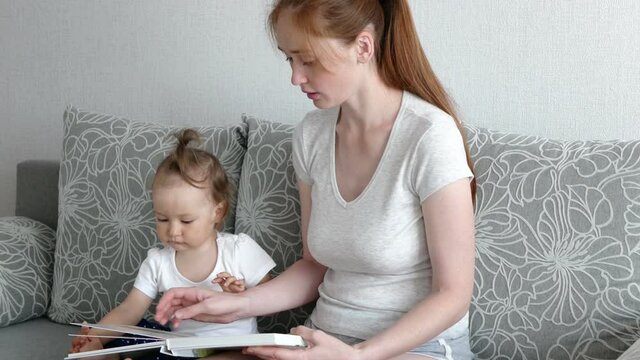 Cute daughter and attractive mother watch photo book. Young mother shows photos her daughter.