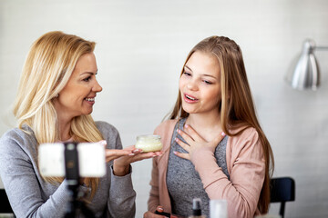 Mother with her daughter recording video blog with mobile phone at home