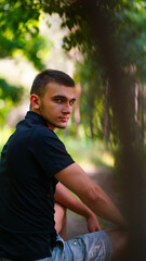 Young handsome man in black shirt and shorts sitting on stump in park