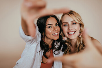 Adorable tanned sisters making selfie. Indoor shot of good-humoured latin lady chilling with friend.