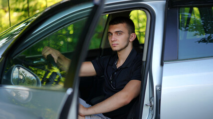 Young handsome man in black shirt and shorts sitting in car
