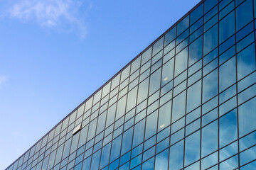 Low angle view of modern office building covered with glass. Blue sky with some white clouds in the background. Corporate Buildings Theme.