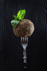 Soft dessert cheese with French herbs on a fork. Photo on a black background. Mint leaves on top. Copy of the space. Vertical photo.