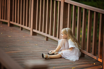 Happy stylish little girl with blonde hair sitting alone on the wooden bridge in the park. The end of COVID-19 Pandemic crisis and lockdown. happiness and hope, stop virus spreading.