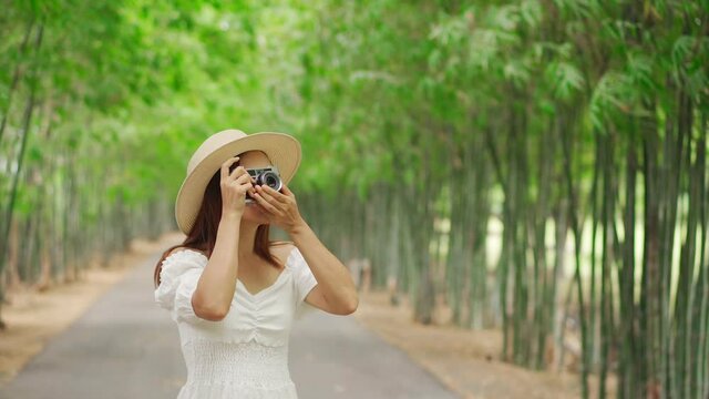 Young happy woman enjoying and taking a photo in the bamboo forest while traveling in summer