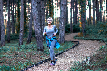 Aged woman jogging in park between woods at the end of day and smile