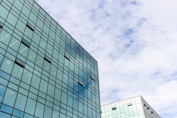Low angle view of modern office building covered with glass. Blue sky with some white clouds in the background. Corporate Buildings Theme.