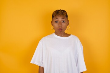 Shot of pleasant looking Young African American girl with afro short hair wearing white tshirt  pouts lips, looks with green eyes at camera,  has fun with girlfriend, Human facial expressions