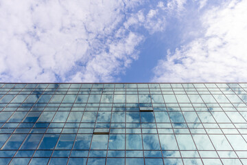 Low angle view of modern office building covered with glass. Blue sky with some white clouds in the background. Corporate Buildings Theme.