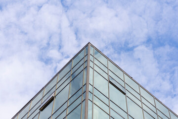 Low angle view of modern office building covered with glass. Blue sky with some white clouds in the background. Corporate Buildings Theme.