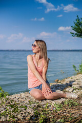 Fototapeta na wymiar A girl sits on a rocky lake shore on a sunny day