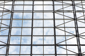 View from below on glass roof in building. Abstract background. Clouds on the sky are visible through glass.
