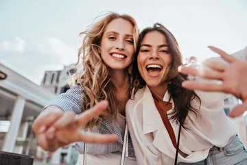 Fotobehang Lovable caucasian girls expressing positive emotions to camera. Outdoor photo of refined sisters posing on sky background. © Look!