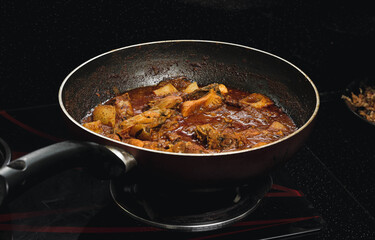 chicken curry is prepared in a pan on a stove.