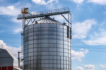 Modern Granary elevator. Silver silos on agro-processing and manufacturing plant for processing drying cleaning and storage of agricultural products, flour, cereals and grain.