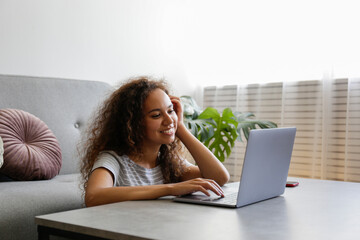 Portrait of young woman with dark skin and long curly hair using her laptop computer. African american female on video call. Freelancer at home office. Close up, copy space, background.