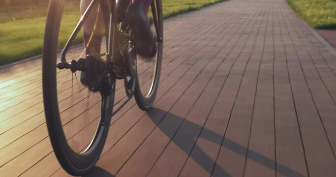 Bike wheel rotation in sunset light. Woman is pedaling bike at sunrise, close up of bike gear. Cyclist twists pedals on bicycle on cycle path at sunset. Cycling gear, chain and cassette. Sport concept