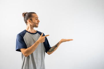 Hombre con moño, caucásico, con camiseta gris de mangas y cuello azul oscuro, señala hacia algo...