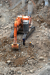 Excavator on the stone ruins after the demolition of a dilapidated house. Vertical photo