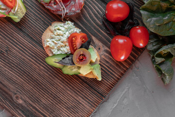 bruschetta with guacomole, cucumber, olives and cherry tomatoes, spinach leaves nearby. top view, flat lay, copy space