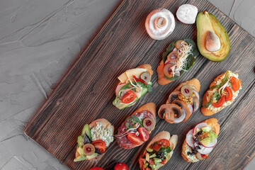 various beautiful bruschettas with vegetables, avocado, salami, cheese, tomatoes, guacamole, olives and radishes on the