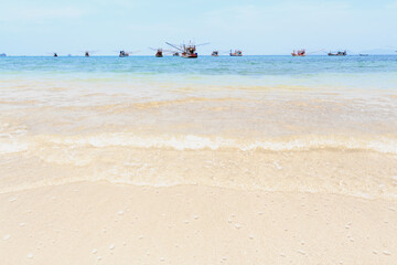 The waves had a clean white bubble lapping the sandy beach, With the backdrop of a group of fishing boats.There is an island behind. The clear blue sky in the summer is perfect to travel.