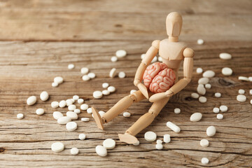Toy man holds brain in his hands, sits next to pills. Treatment of headache and depression. Drug...