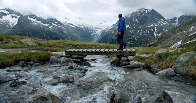 Male hinke in alpine mpountains crossing river with mountains in background. Outdoor active lifestyle concept