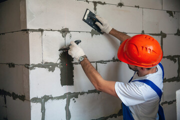 Mason aligning aerated autoclaved concrete block of constructed house wall