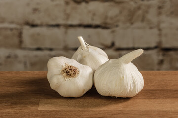 Drei Knollen Knoblauch / Knoblauchzwiebeln auf einem hölzernen Hintergrund vor einer Mauer aus Stein