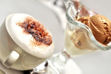 Cup of cappuccino with milk foam sprinkled with cinnamon and chocolate ice cream on a cafe table