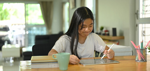 A schoolgirl is using a white blank screen computer tablet and stylus pen at the sitting room.